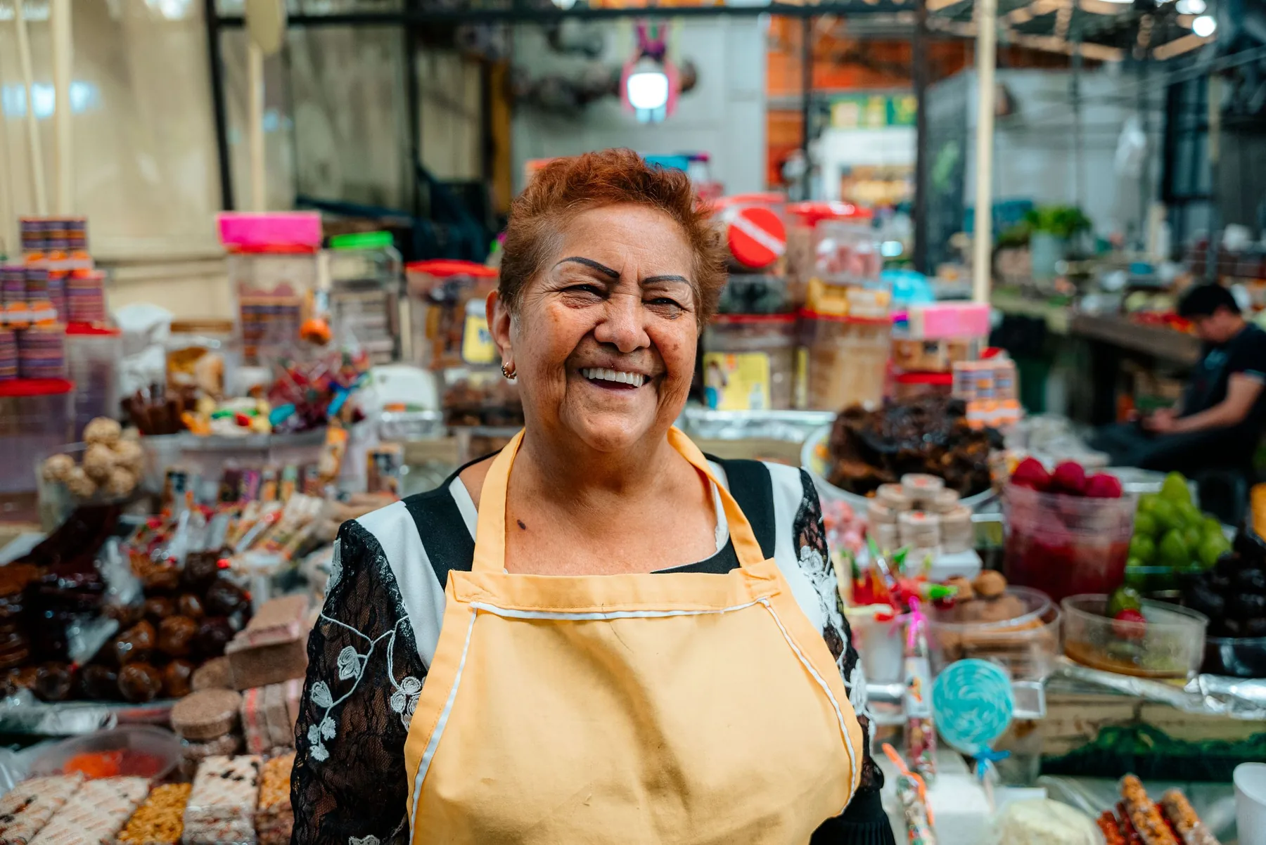 Dueña de un puesto de mercado, con delantal, sonriendo entre sus productos
